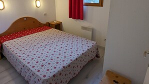 A bedroom with a bed, a nightstand, a window with a red curtain, and a wall-mounted heater.