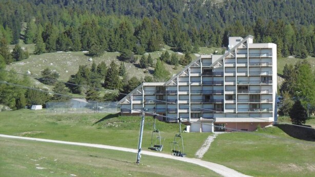 Un hotel de varios pisos con un diseño arquitectónico moderno, situado en una zona montañosa donde se ve un telesilla en primer plano.