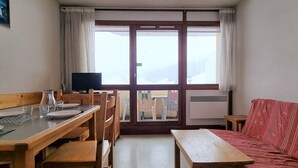Una habitación con una mesa de comedor de madera, sillas, un sofá rojo, un televisor y un ventanal con cortinas.