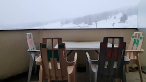Un balcón con mesa y sillas, con vista a un paisaje montañoso nevado.