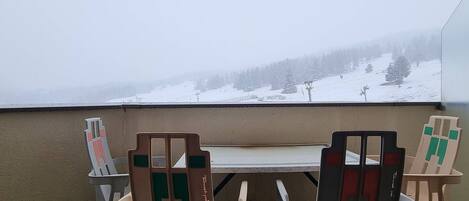 Un balcón con mesa y sillas, con vista a un paisaje montañoso nevado.