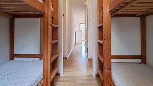 Een smalle gang met houten stapelbedden aan weerszijden, die uitkomt in een lichte kamer.