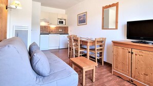 A compact living space with a sofa, a dining table with chairs, a television, and a kitchen area with a microwave.