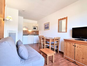 Um espaço de estar compacto com sofá, mesa de jantar com cadeiras, televisão e cozinha equipada com micro-ondas.