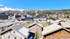 A mountain town with modern and traditional buildings, a ski slope, and snow-capped mountains in the background.