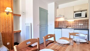 A compact kitchen with white cabinets, a microwave, and a dishwasher. There is a dining table with chairs and a lamp.