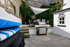 A patio with a barbecue grill, outdoor seating, and a white wall with a window. - Beautiful House in Bideford on Peaceful Street (Bideford)