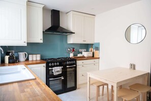 Una cocina compacta con armarios blancos, una estufa negra y una mesa de madera con sillas.
