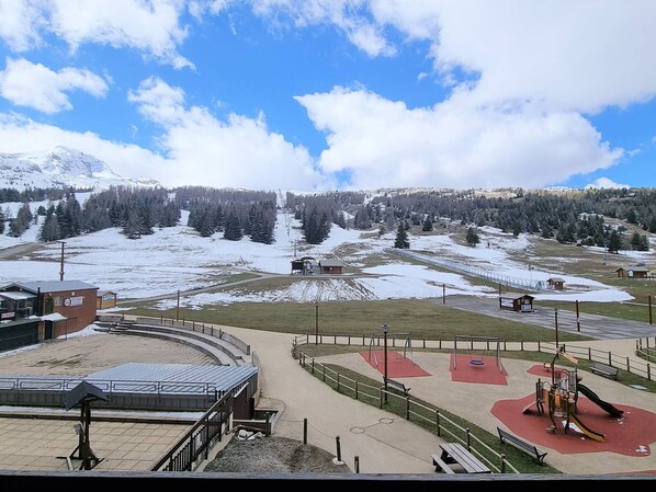 A ski resort with a playground, a small building, and a view of snow-covered mountains.