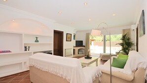 Een woonkamer met een beige bank, een witte bank, een bijzettafeltje en een vloerlamp.