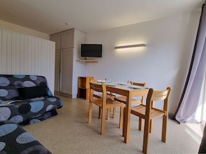 Quarto com sofá, mesa de jantar com cadeiras, televisão na parede e armário.
