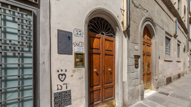 Un edificio con un gran puerta doble de madera, una pequeña placa con el número 53, y una ventana con celosía de metal.