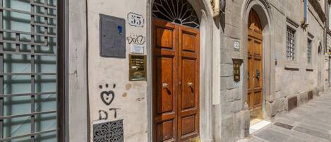 A building with a large wooden double door, a small plaque with the number 53, and a window with a metal grille.