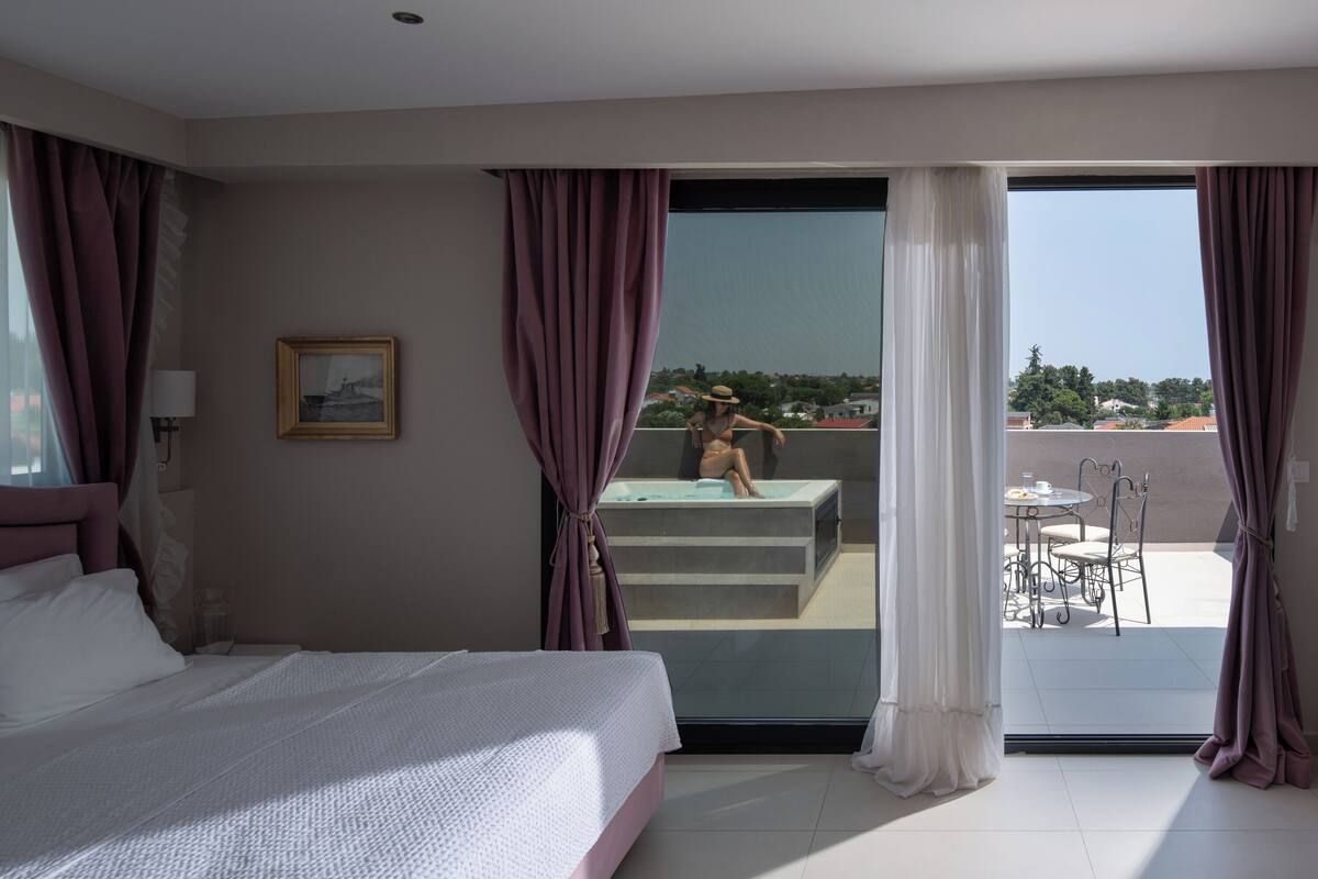 A bedroom with a bed, a window, and a balcony with a table and chairs.