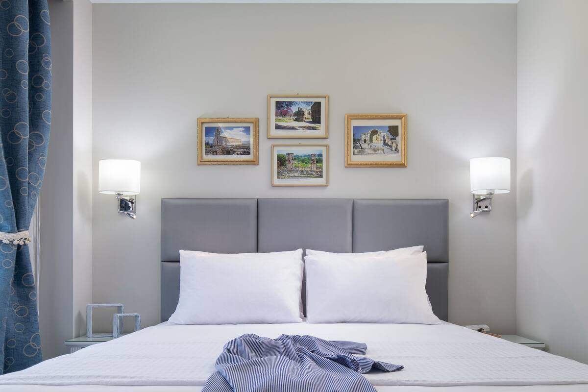 A hotel room with a large bed, two wall-mounted lamps, and three framed pictures on the wall.