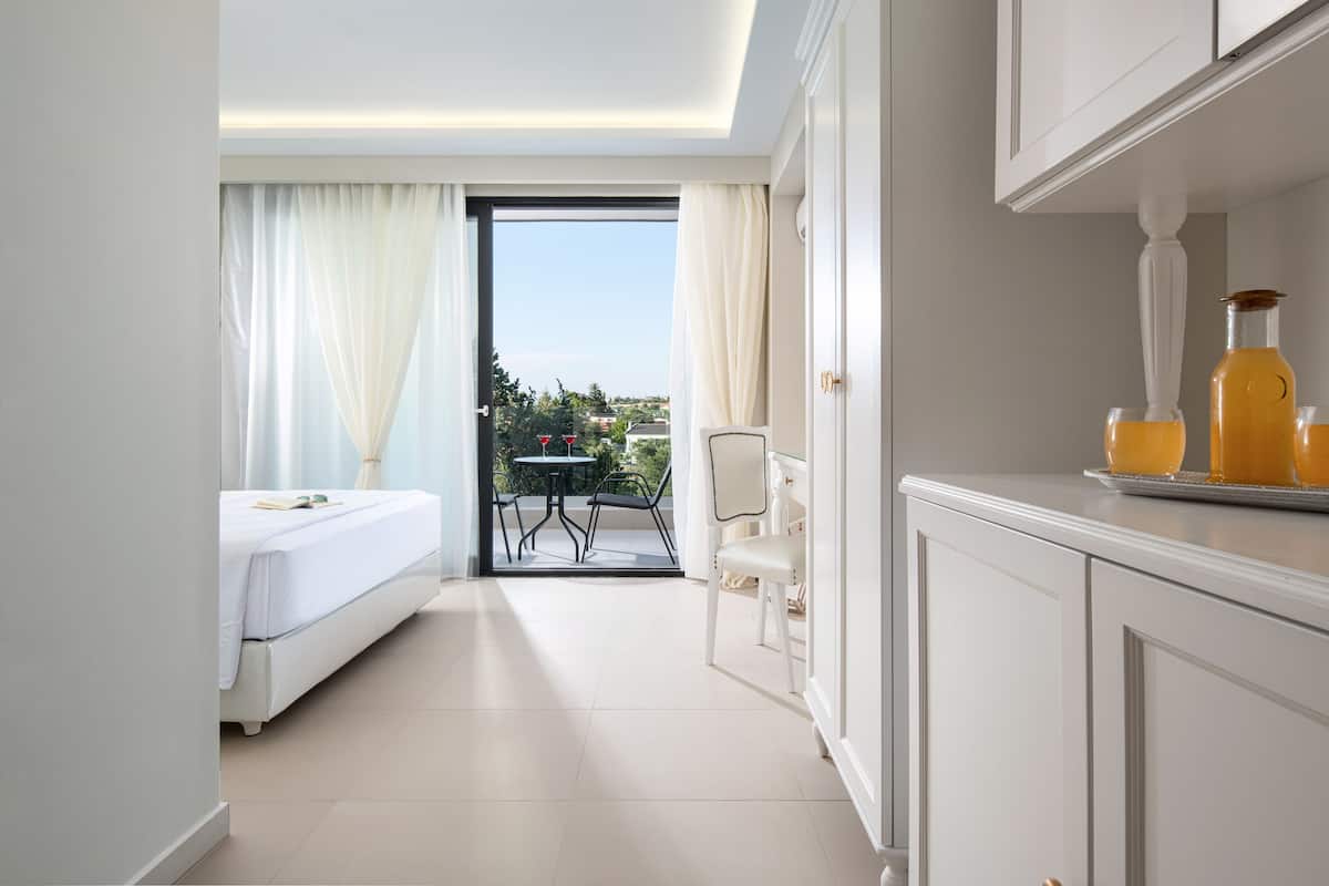 A hotel room with a bed, a dining table with chairs, and a view of the outdoors.