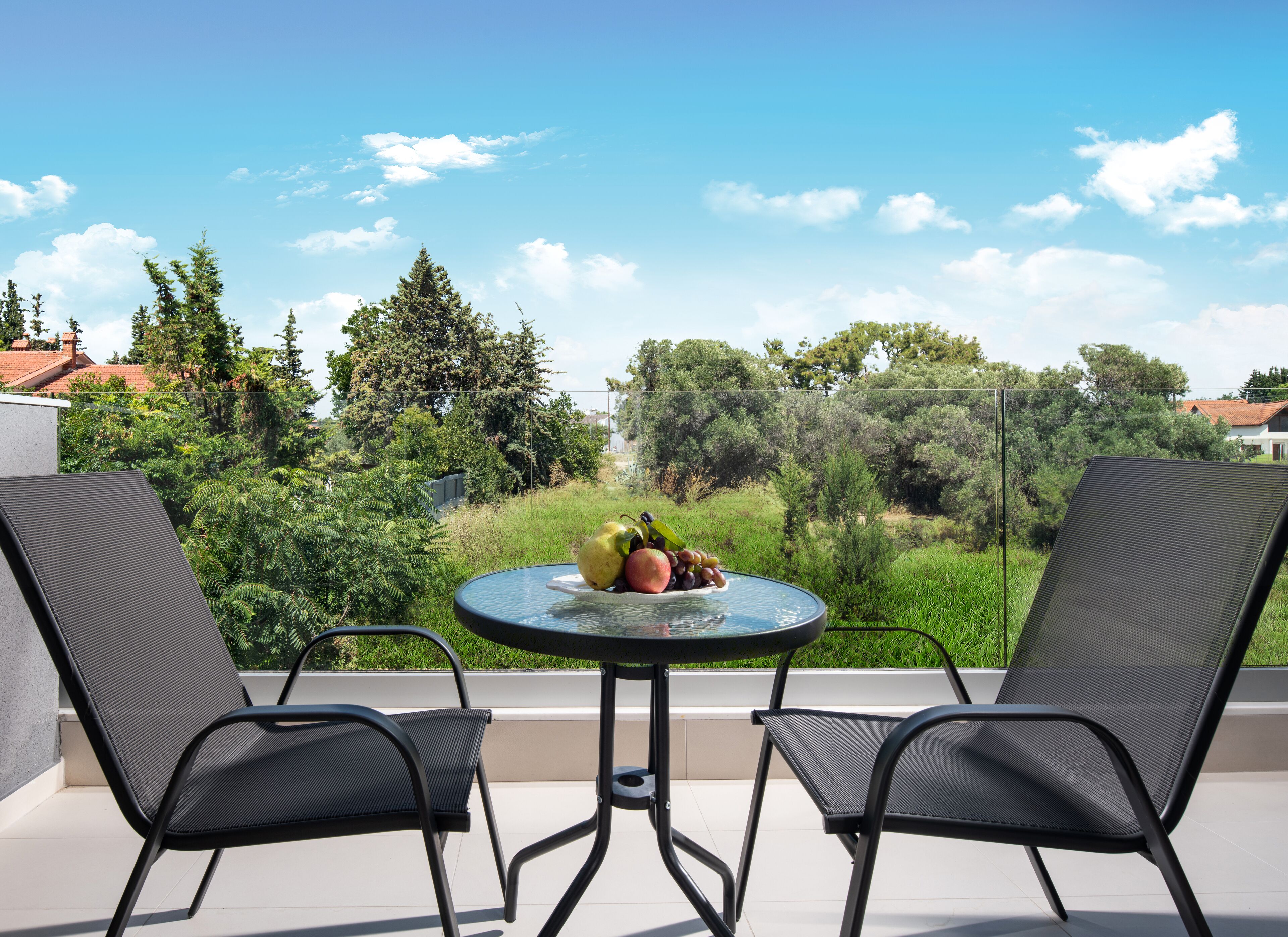 A balcony with two chairs and a table, overlooking a lush green landscape and a clear blue sky.