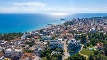 An aerial view of a coastal town with buildings, a clear blue sea, and a distant pier.
