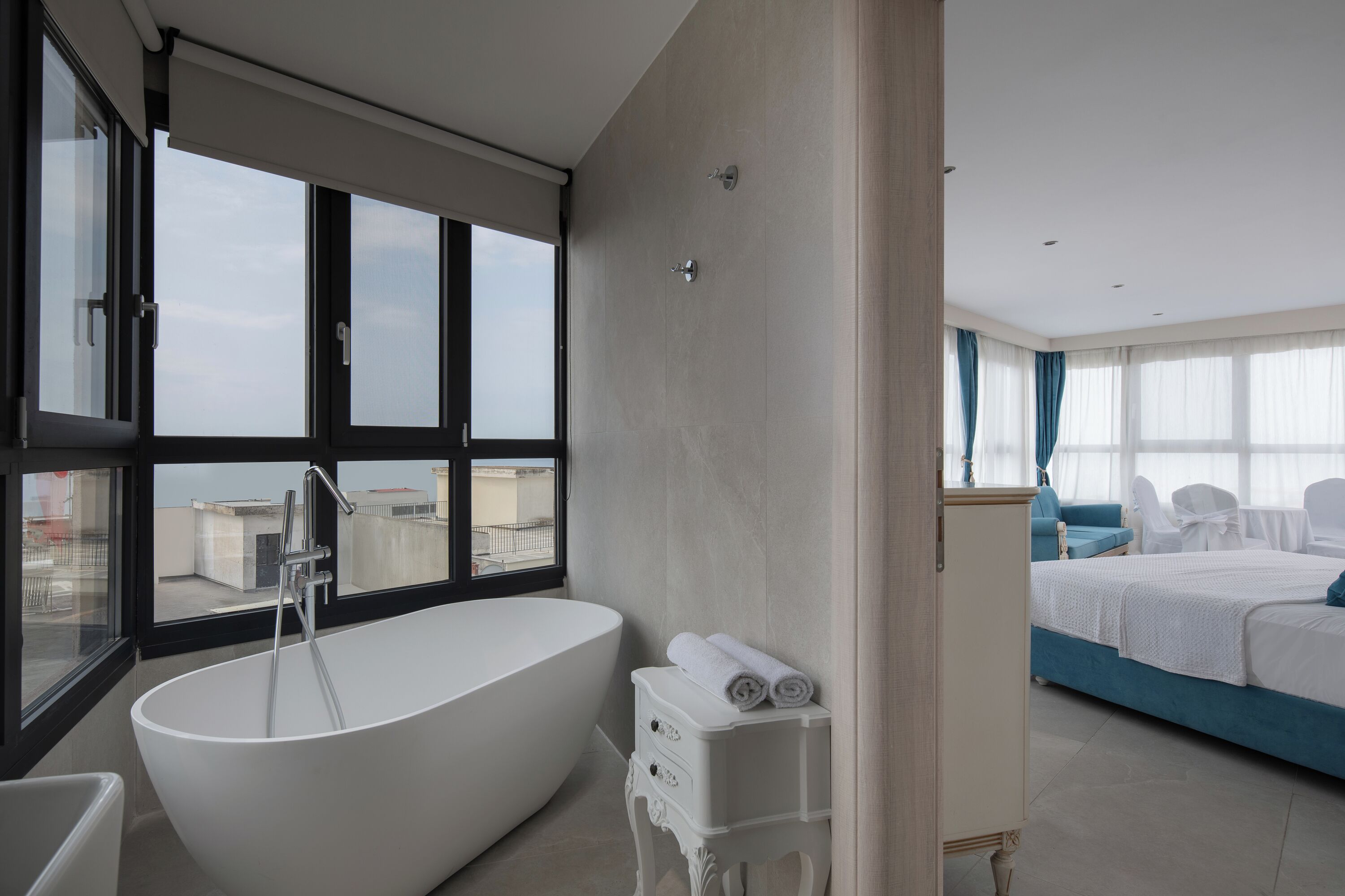 Un baño moderno con una bañera independiente, un tocador con espejo y un ventanal con vistas a la ciudad.