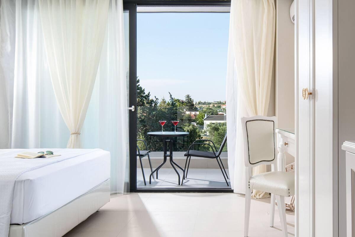 A bedroom with a bed, a chair, a small table, and a balcony with a table and chairs.