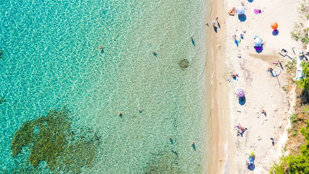 An aerial view of a beach with clear turquoise water, people swimming, and beach umbrellas. - Light Blue Luxury Rooms (Nea Propontida)