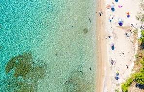 An aerial view of a beach with clear turquoise water, people swimming, and beach umbrellas. - Light Blue Luxury Rooms (Nea Propontida)