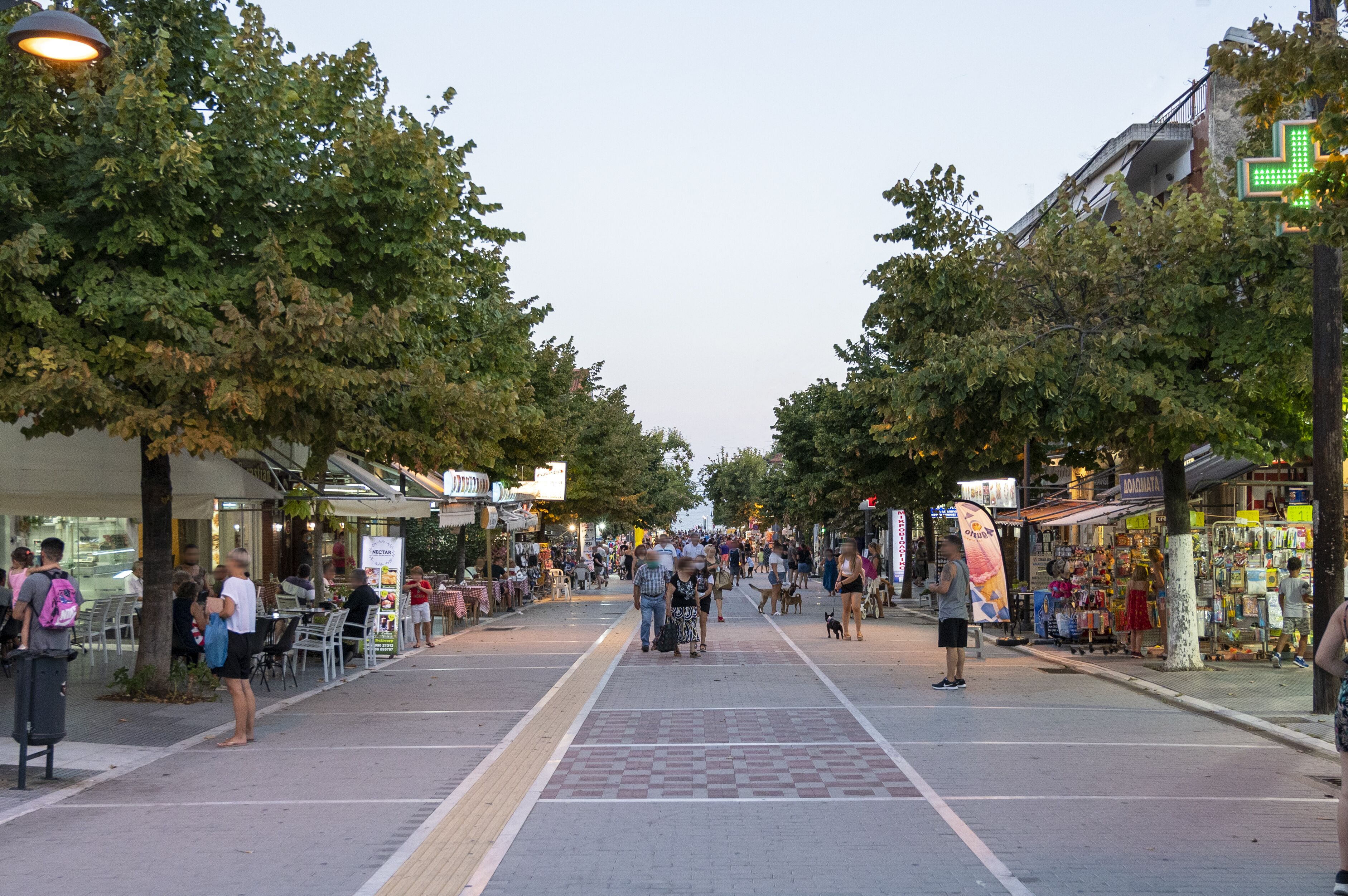 En livlig stadsgata kantad av butiker och kaféer, med en gångbana och träd.