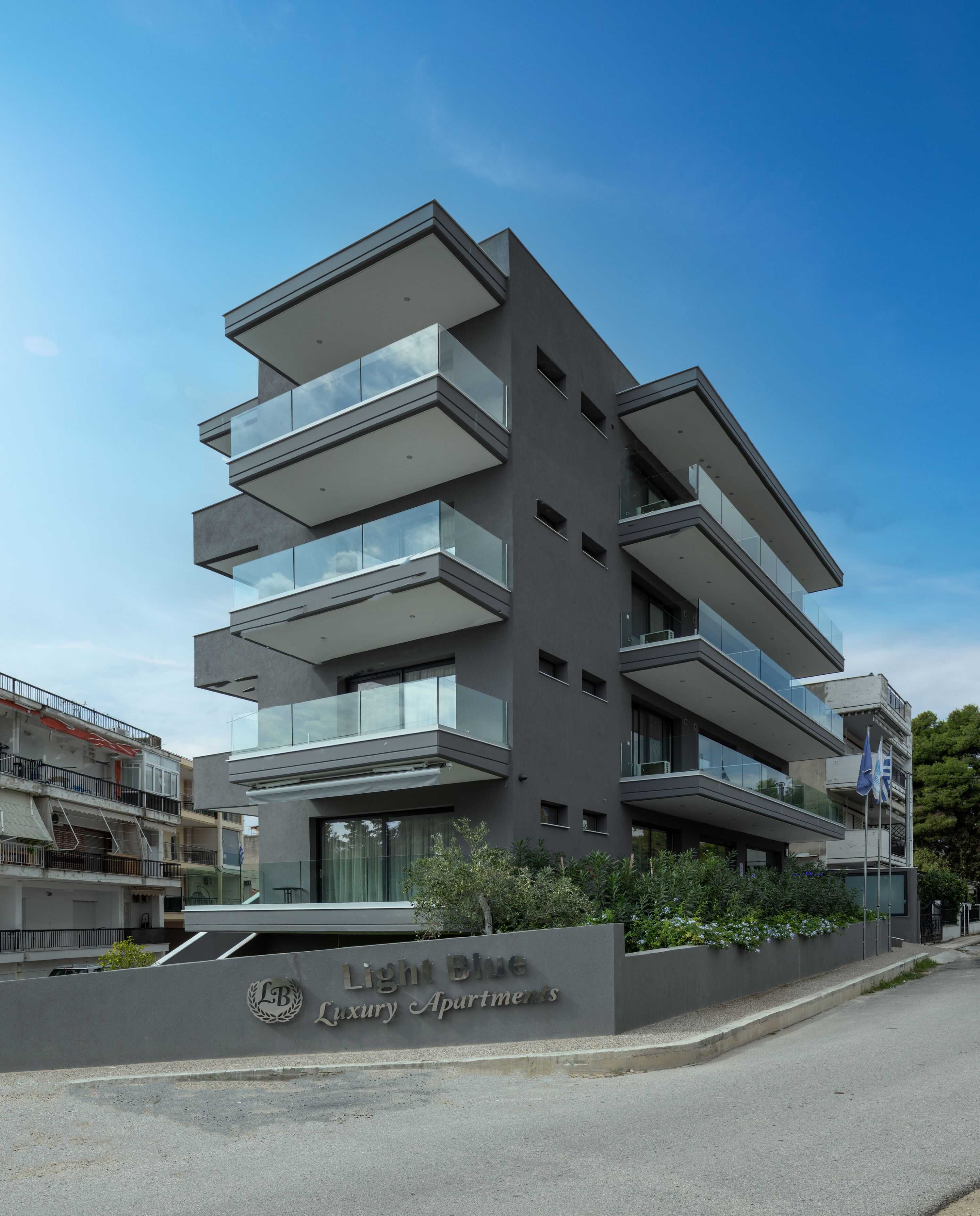 A multi-story building with balconies, a sign reading "Light Blue Luxury Apartments," and a clear sky.