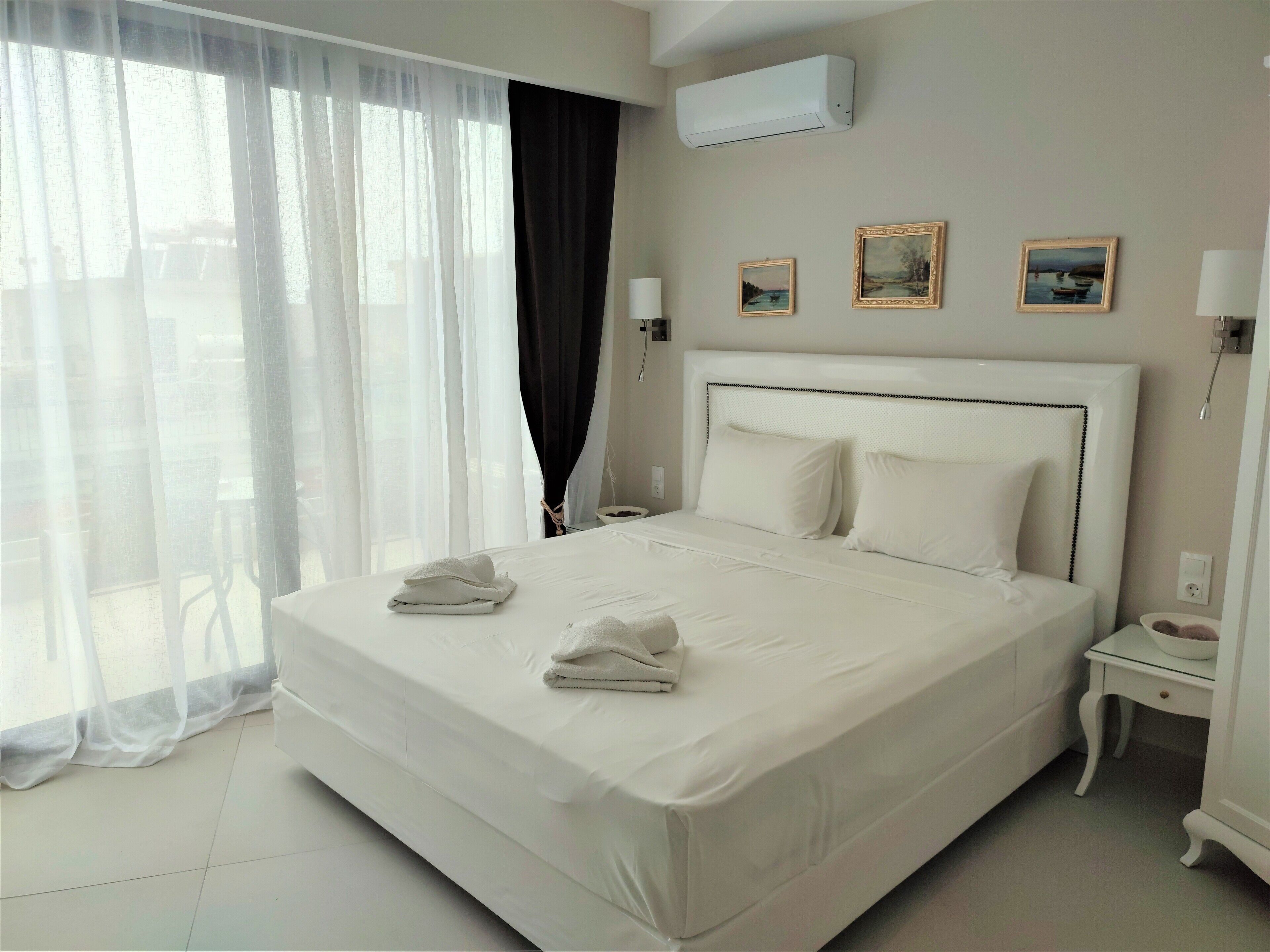 A hotel room with a large bed, a bedside table with a lamp, and a window with sheer curtains.