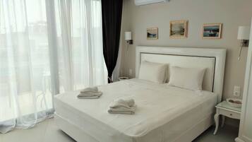 A hotel room with a large bed, a bedside table with a lamp, and a window with sheer curtains.