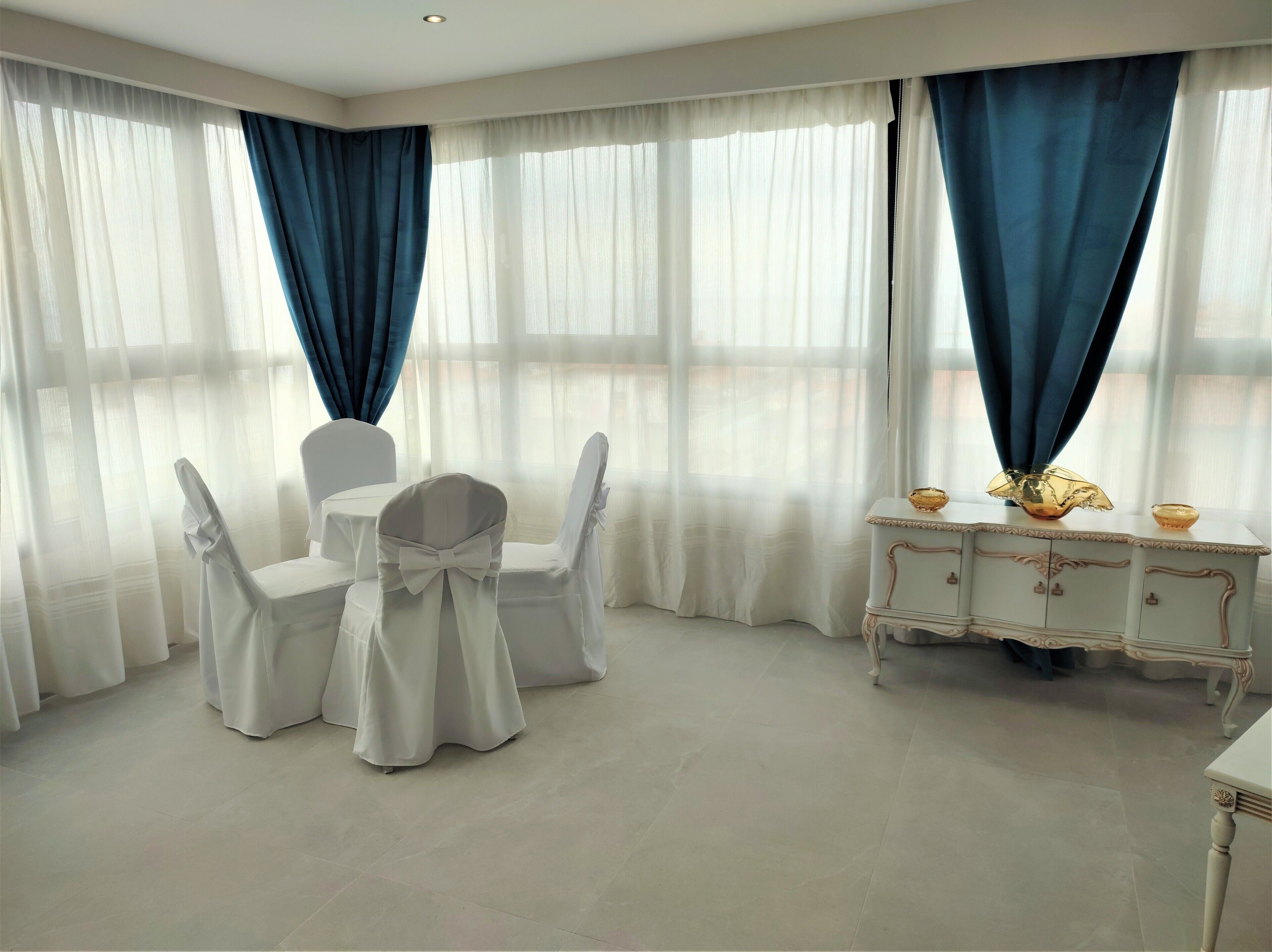 Ein Zimmer mit Tisch, Stühlen, einem weißen Schrank und blauen Vorhängen.