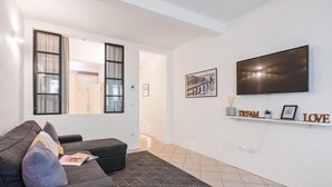A living room with a sofa, a TV, and a shelf with decorative items.
