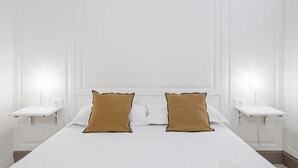 A hotel room with a large bed, two bedside tables, and wall-mounted lamps.