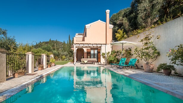 Une piscine dotée de chaises longues et d’une pergola, entourée d’un jardin et d’un bâtiment avec un balcon.