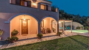 Une maison à deux étages dotée d’un patio couvert, d’une piscine et d’un chemin de pierre menant à l’entrée.