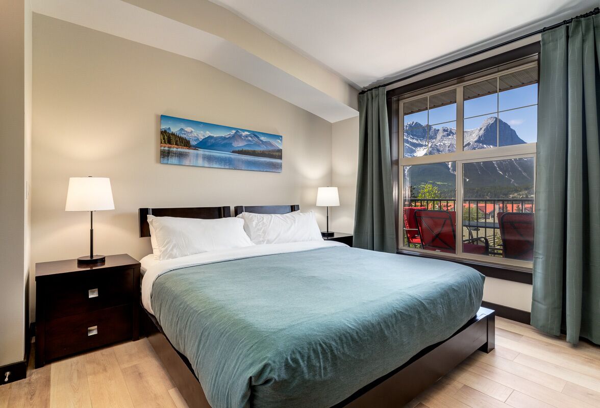Ein Schlafzimmer mit einem großen Bett, zwei Nachttischen, einem Gemälde von einer Berglandschaft und einem Fenster mit Bergblick.
