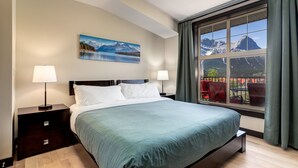 Una camera da letto con un letto grande, due comodini, un quadro che raffigura un paesaggio montano e una finestra con vista sulle montagne.