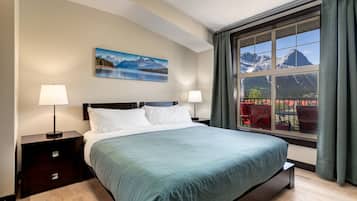Ein Schlafzimmer mit einem großen Bett, zwei Nachttischen, einem Gemälde von einer Berglandschaft und einem Fenster mit Bergblick.