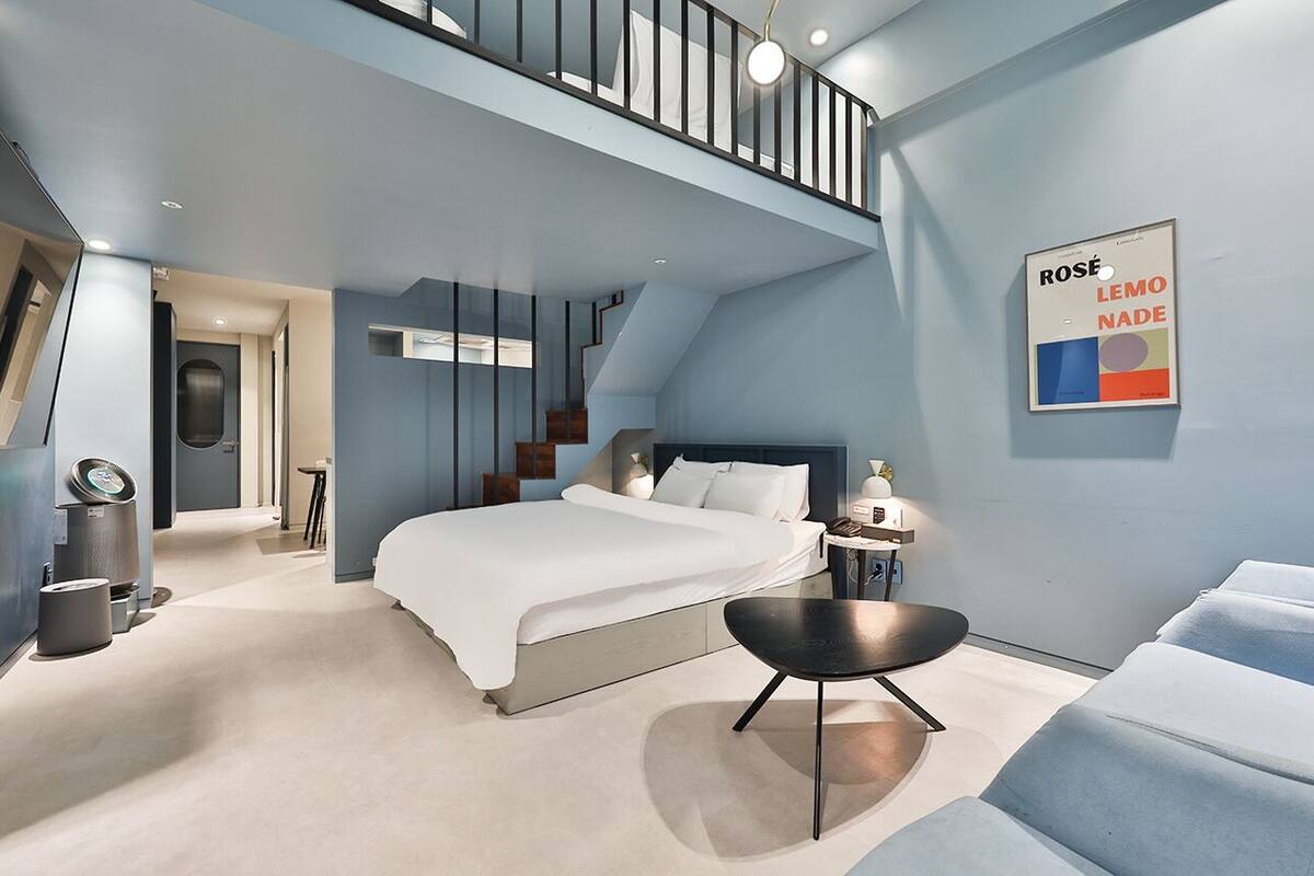 Een moderne slaapkamer met een groot bed, een klein tafeltje, een stoel en een trap naar een hoger niveau.