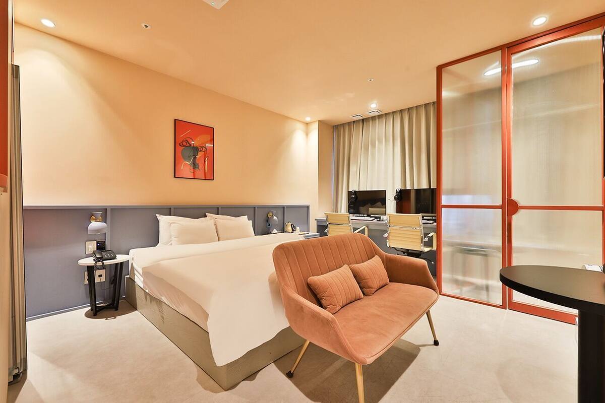 Een hotelkamer met een bed, een stoel, een bureau, een telefoon en een schilderij aan de muur.