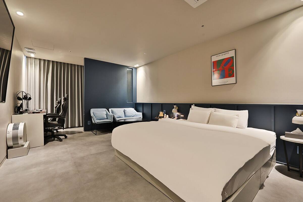 Een hotelkamer met een groot bed, een bureau met stoel, een bank en een kunstwerk aan de muur.