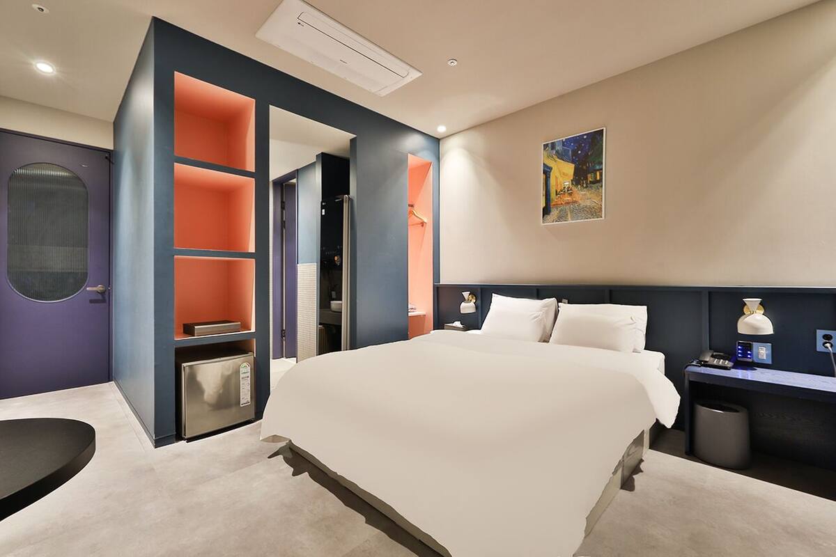 Een moderne hotelkamer met een groot bed, een bureau en een garderobe met oranje accenten.