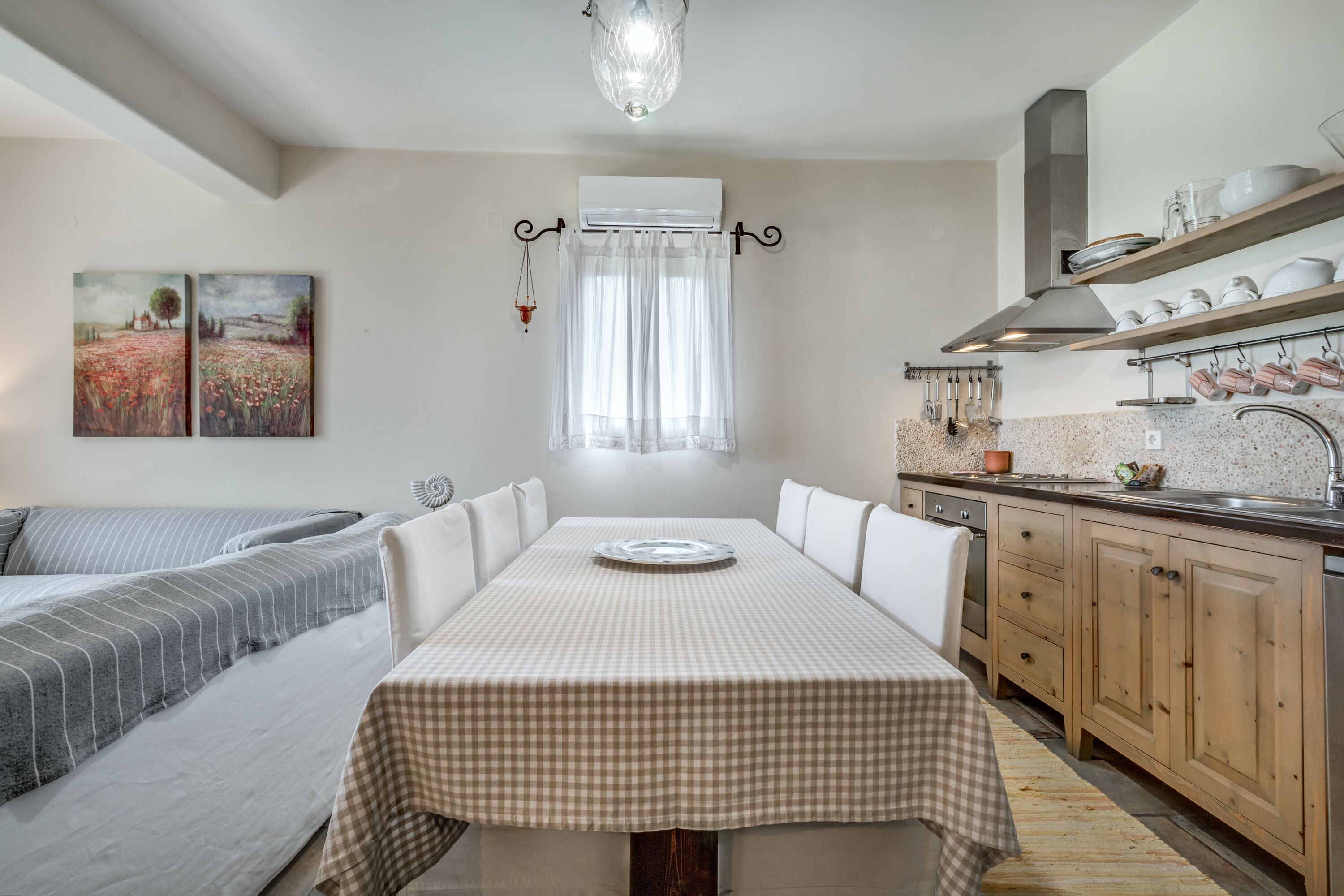 A modern kitchen with a dining table, wooden cabinets, and a window with sheer curtains.