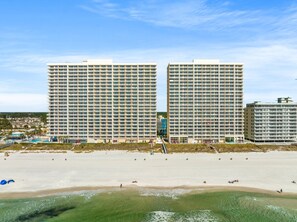 A beachfront hotel with multiple high-rise buildings, a sandy beach, and a clear sky.