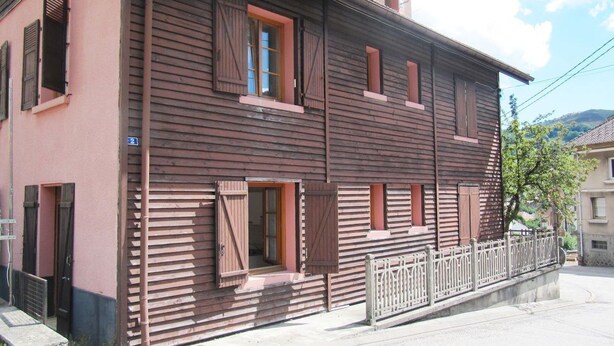 A two-story building with a pink facade and wooden shutters on the windows. - Apartment with a view in the center of Bussang (Bussang)