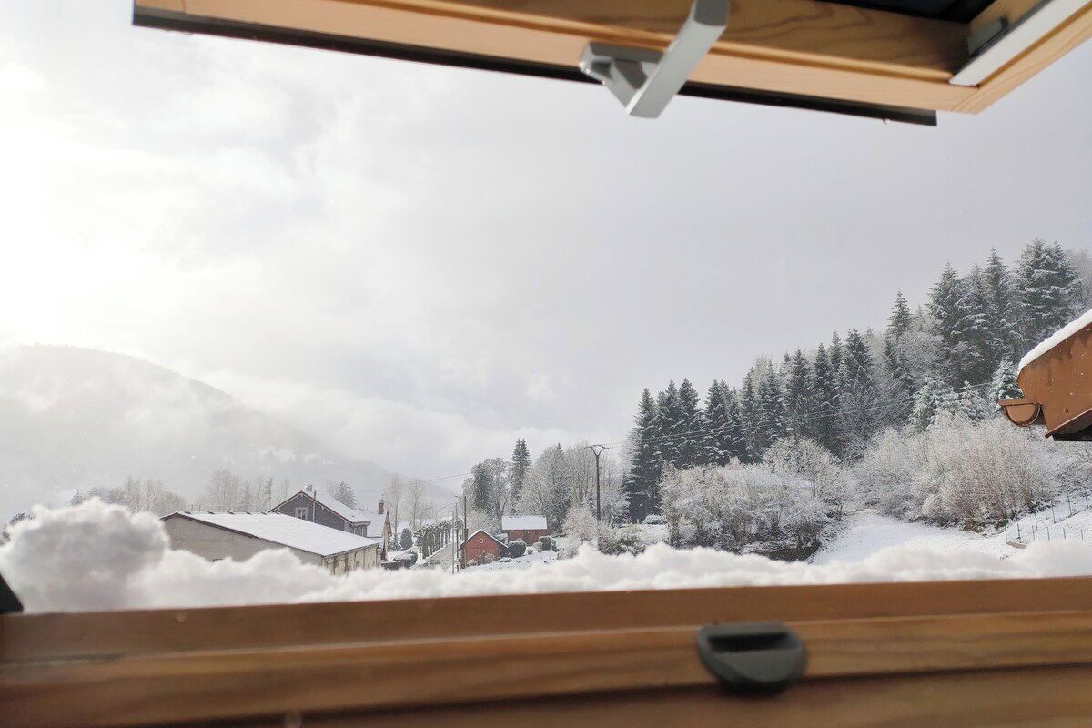 A view from a window with a wooden frame, overlooking a snowy landscape with houses and trees.