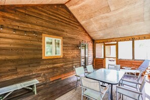 Interior de una cabaña de madera con comedor, banco y ventana con vistas a la vegetación.