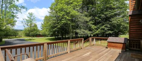 Um deck de madeira com uma cadeira de metal, cercado por árvores e vista para uma estrada.