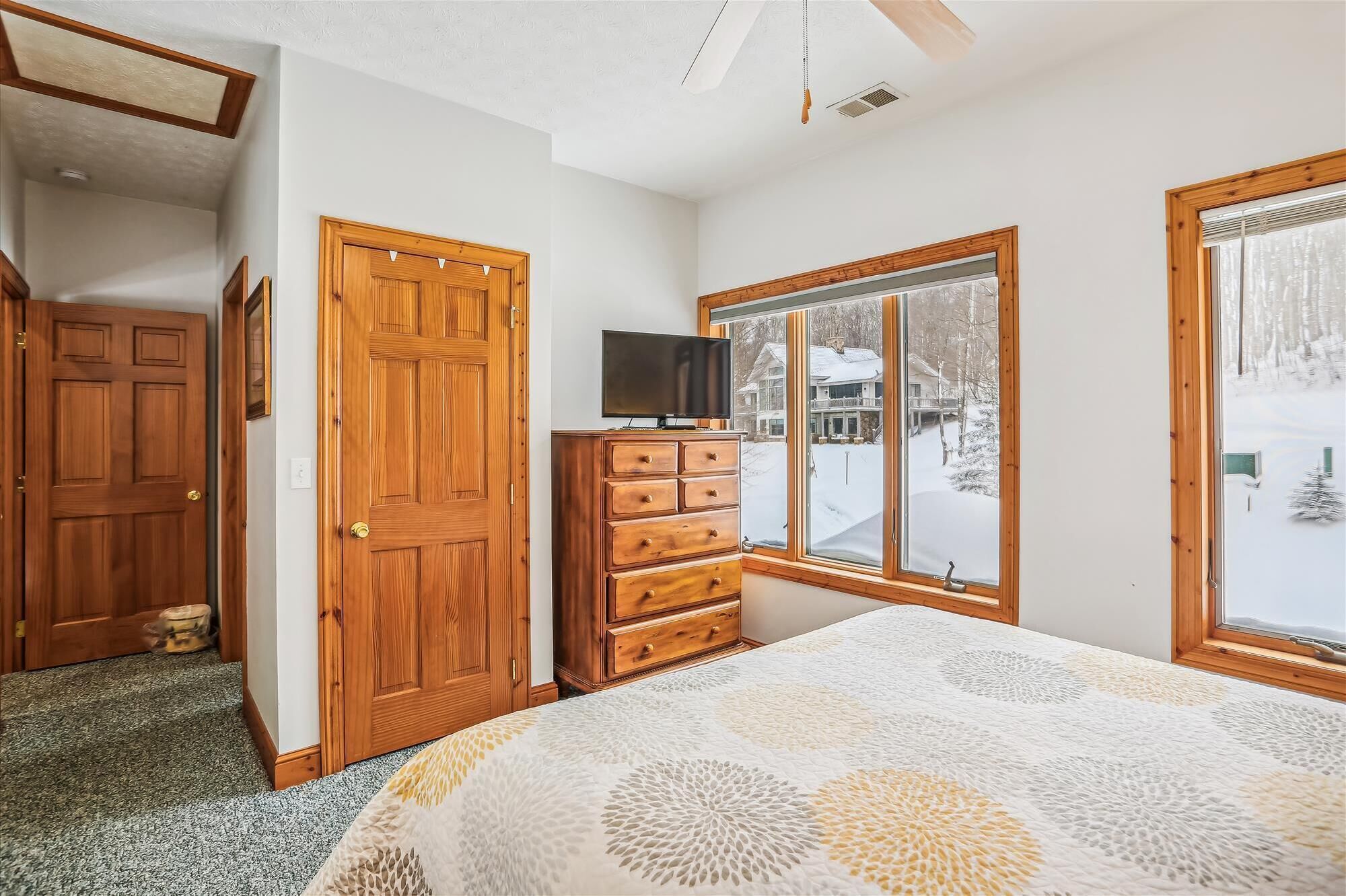 A bedroom with a large bed, a dresser, a television, and a window with a snowy view.