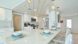A modern kitchen with white cabinets, a central island with blue plates, and pendant lighting. - All Docked Out-Bring Your Own Boat! Private Heated Pool, Free WiFi 3 Mins to AMI (Bradenton)